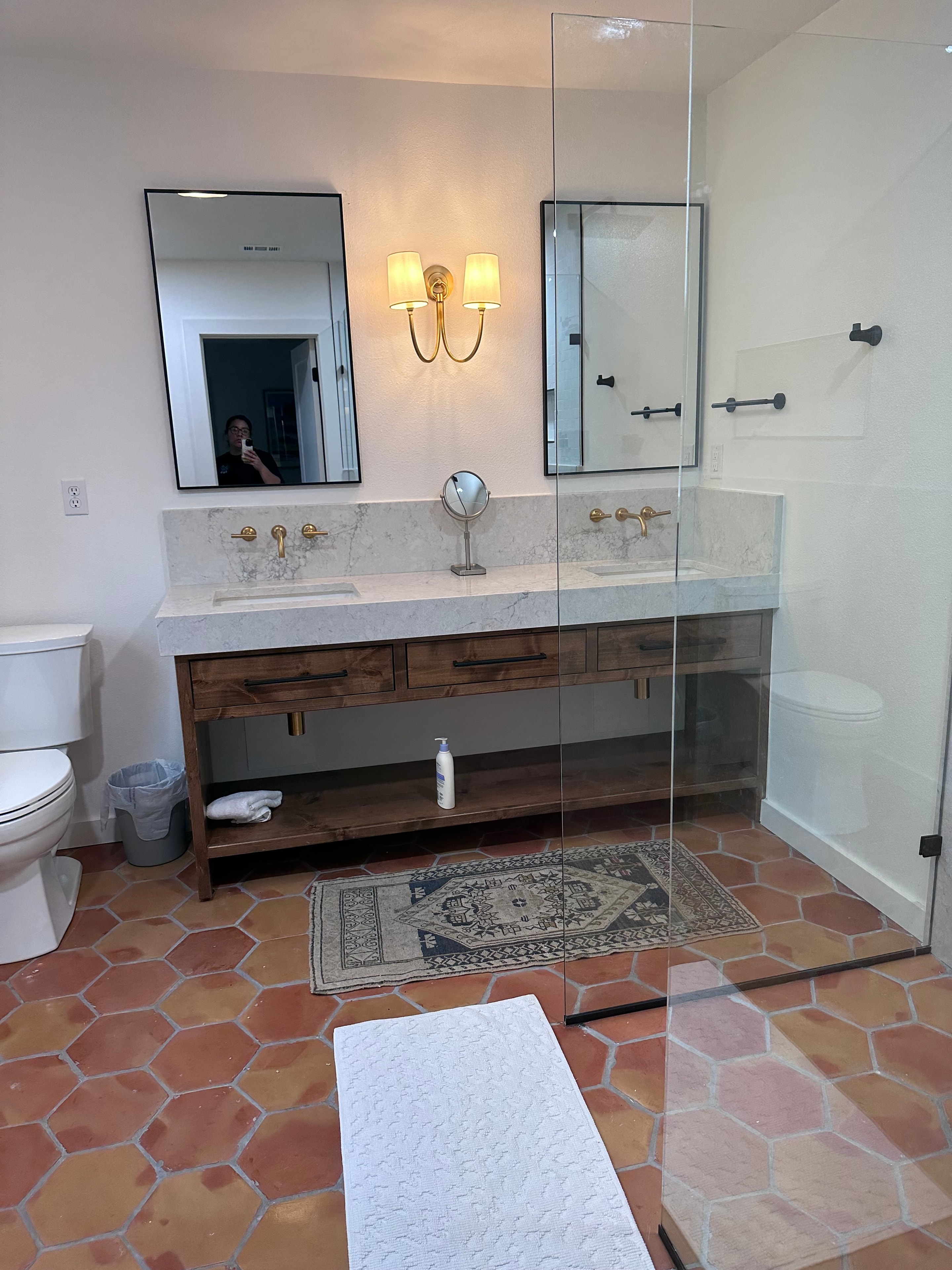 Custom bathroom with terracotta hex tile floor, wood double vanity, and gold sconces