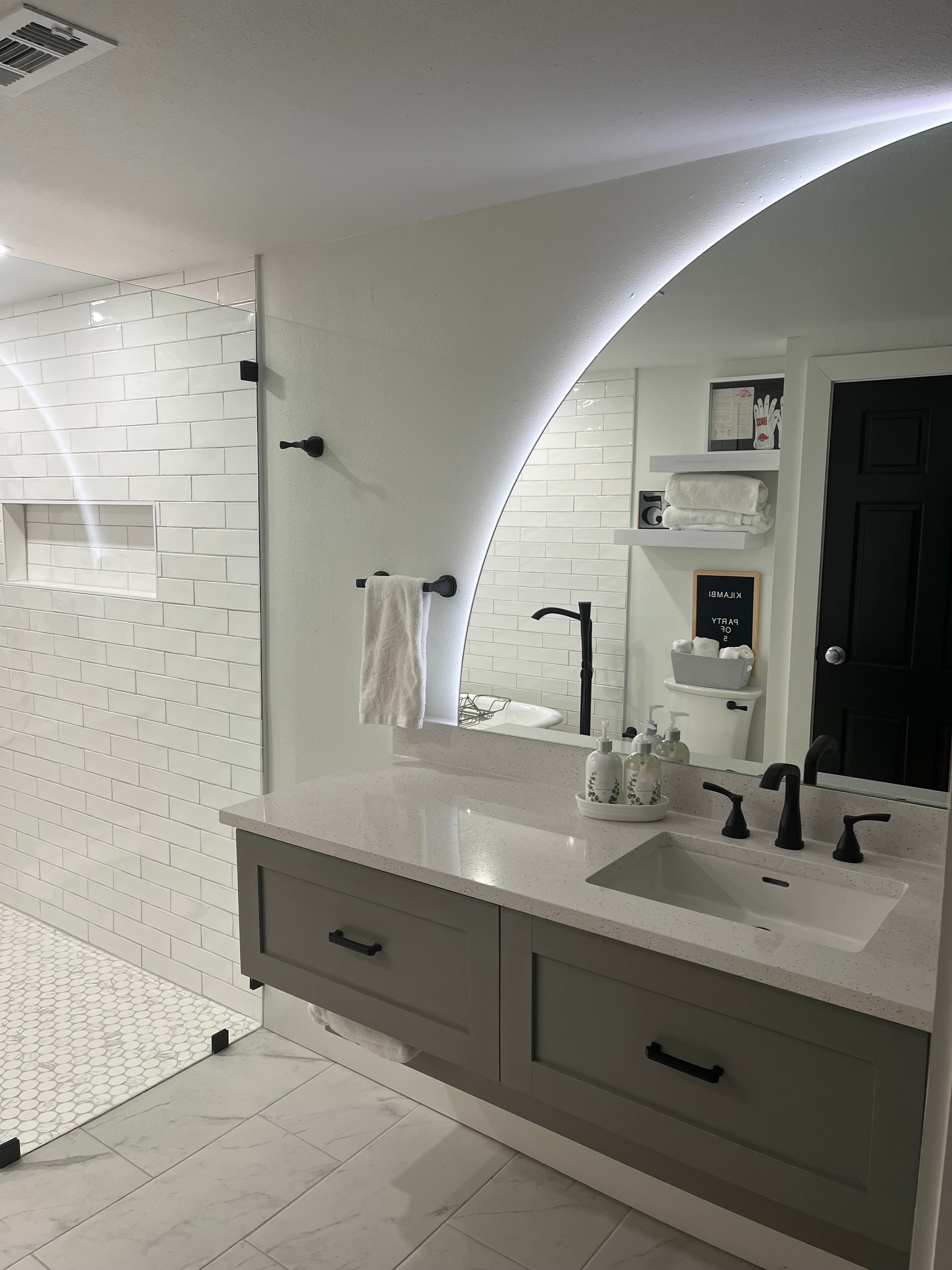 Custom bathroom with LED arc mirror, gray vanity, and white subway tile shower